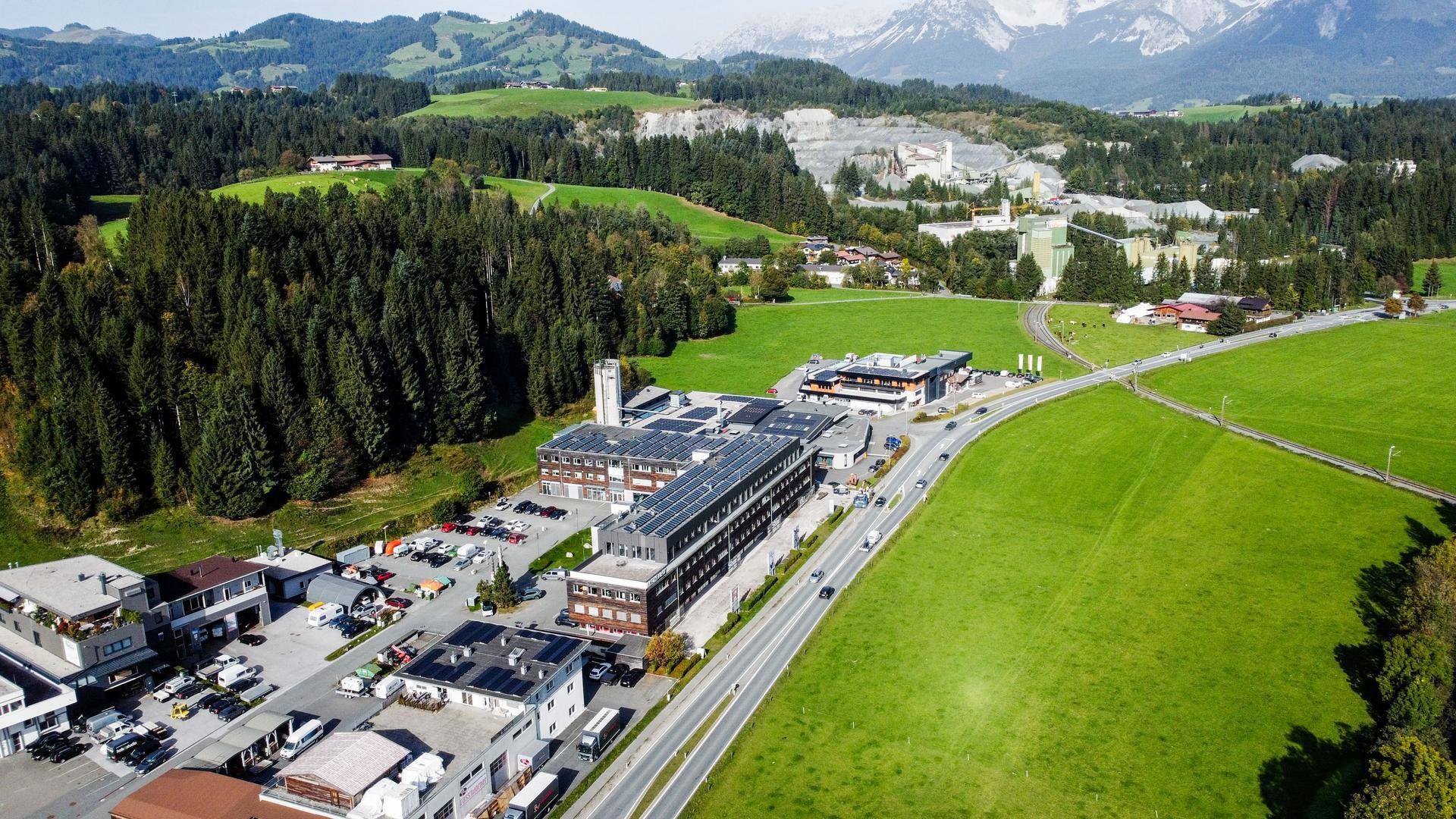 Luftaufnahme eines Gewerbegebiets mit mehreren Gebäuden, Parkplätzen und grüner Umgebung in den Bergen.