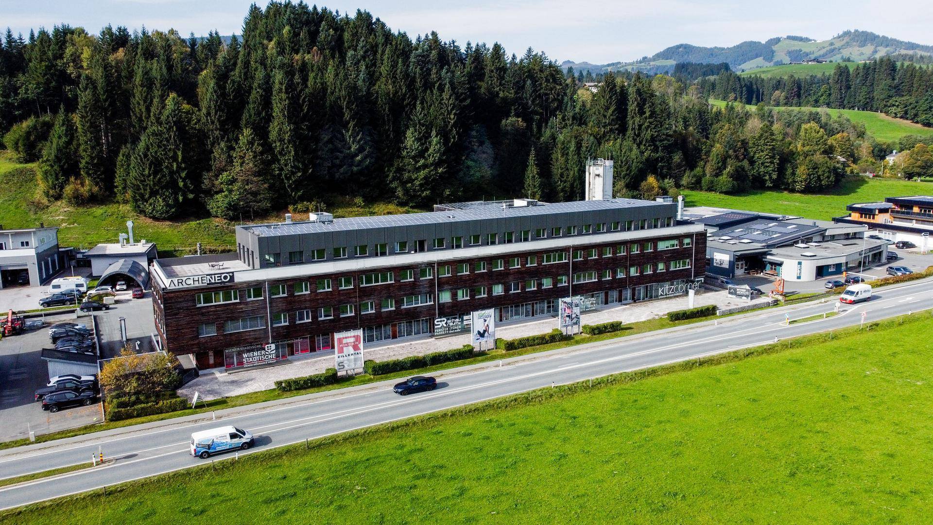 Luftaufnahme eines modernen Geschäftsgebäudes mit Photovoltaikanlage, umgeben von Wald und einer Straße.