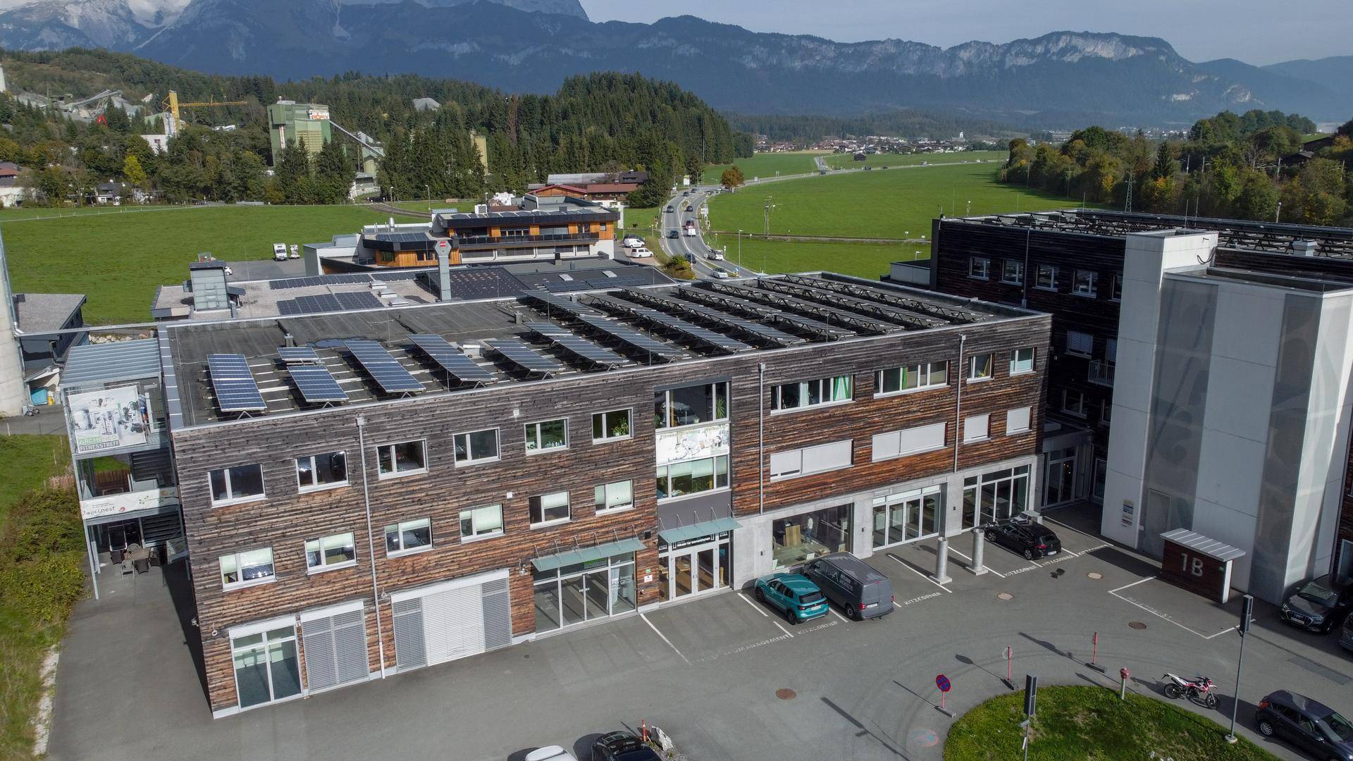Luftaufnahme eines modernen Geschäftsgebäudes mit Photovoltaikanlage und Parkplätzen in ländlicher Umgebung.
