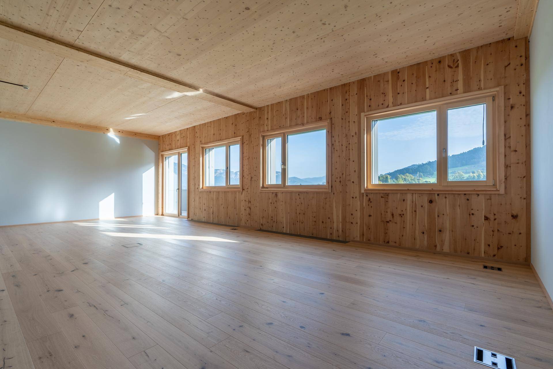 Geräumiger, heller Raum mit Holzwänden und -decke, großen Fenstern und weitem Blick auf die Landschaft.