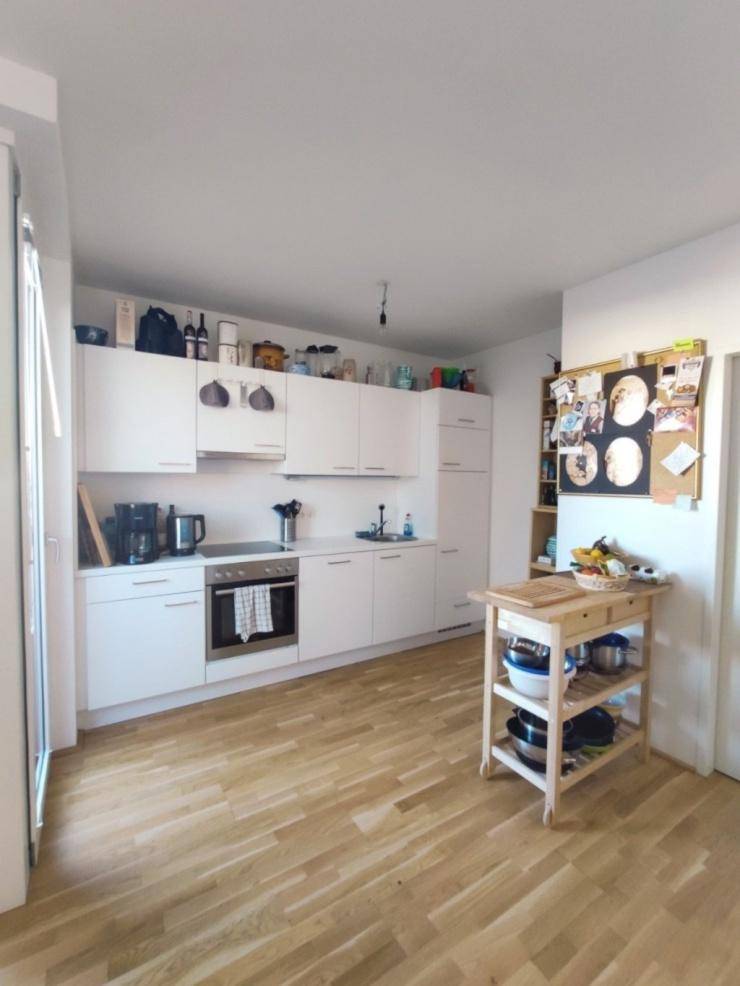 Moderne weiße Küche mit Holzboden, integrierten Geräten und viel Stauraum.