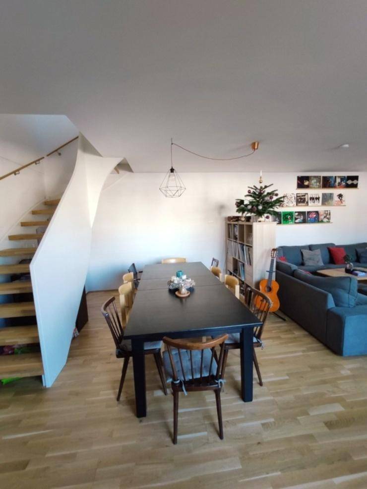 Heller Wohn- und Essbereich mit Holztreppe, großem Esstisch und gemütlichem Sofa.