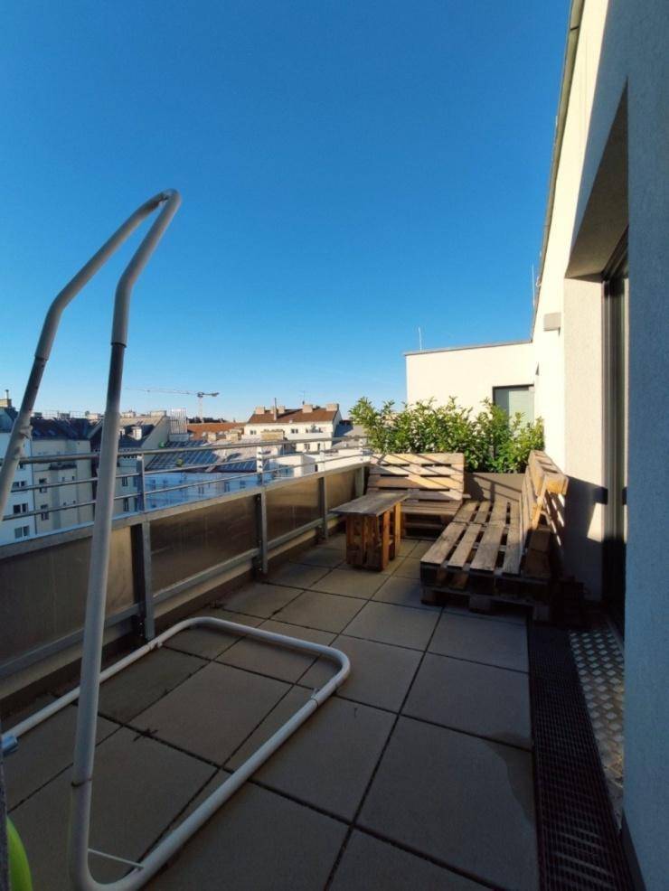 Sonnige Dachterrasse mit Palettenmöbeln und weitem Blick über die Stadt.