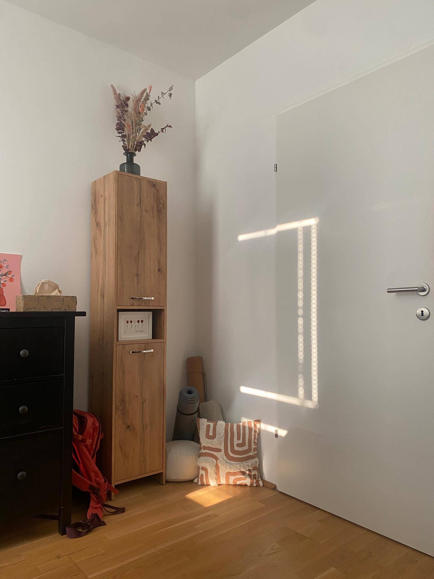 Heller Innenraum mit Holzschrank, weißer Tür und Sonnenlicht, das durch ein Fenster fällt.