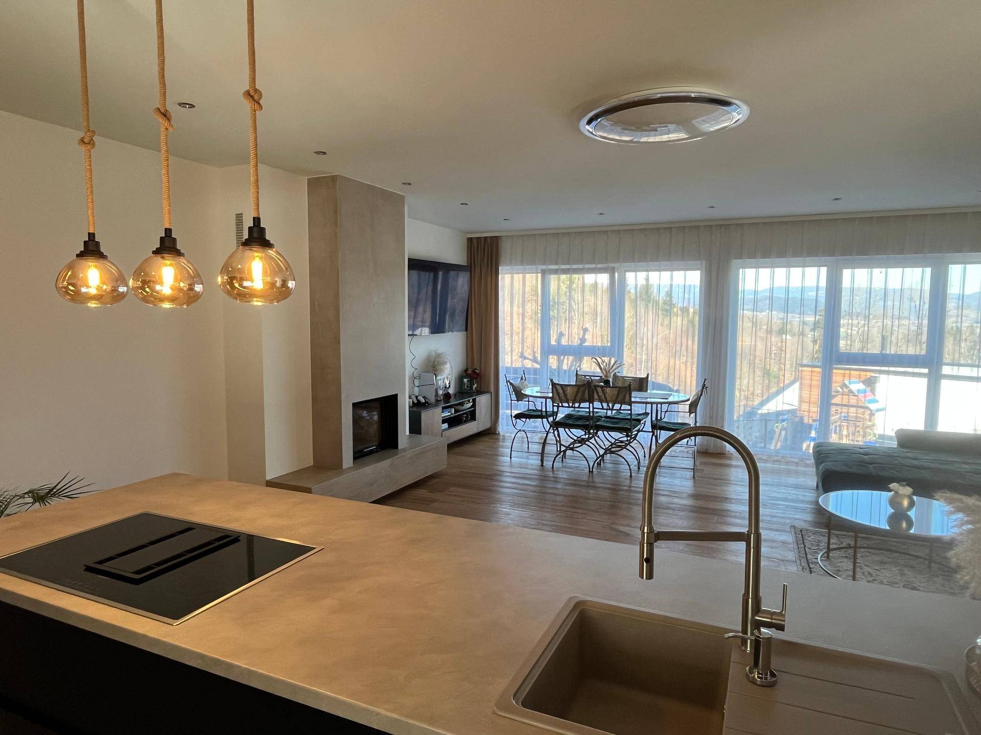 Offener Wohnbereich mit moderner Küche, Kamin und großen Fenstern mit Weitblick.