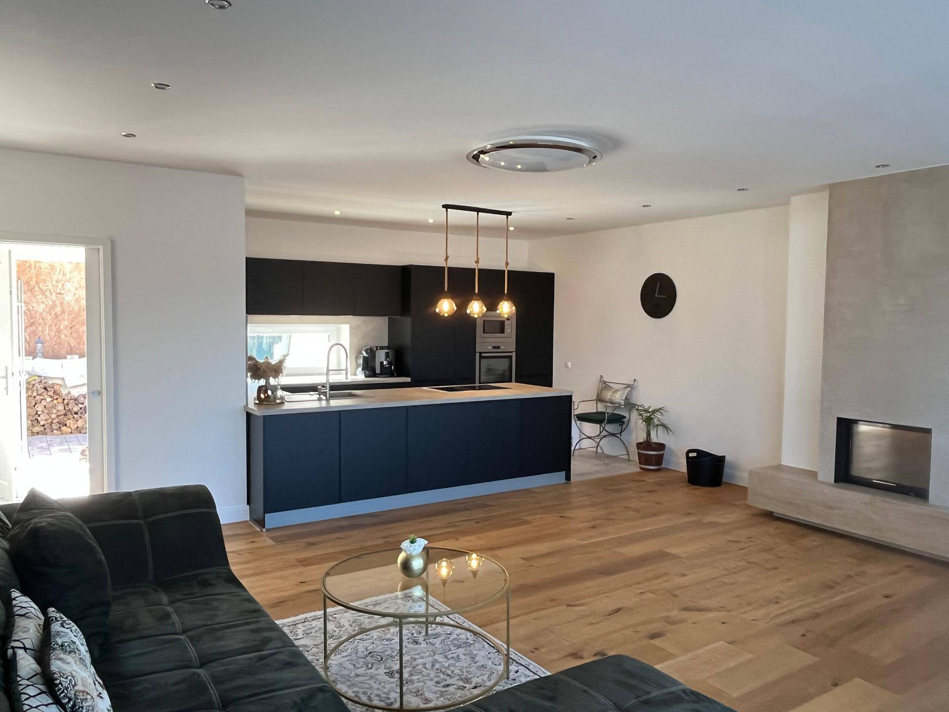 Moderner offener Wohnbereich mit schwarzer Küche, Kamin und Holzboden.