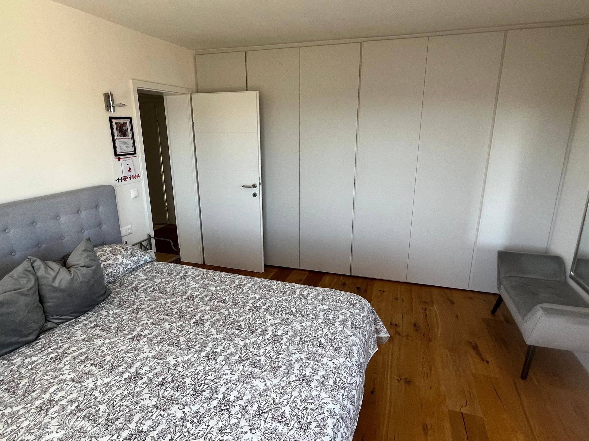 Geräumiges Schlafzimmer mit Holzboden, Doppelbett und einer Wand voller Einbauschränke.