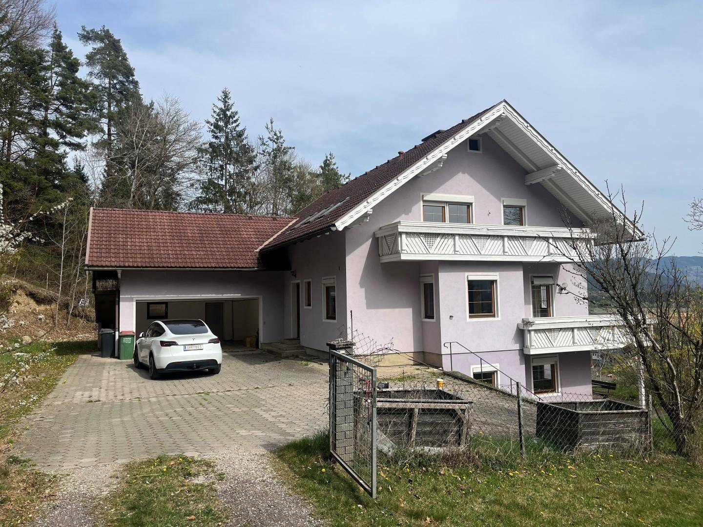 Ansicht des Hauses mit lila Fassade, Satteldach und Carport.