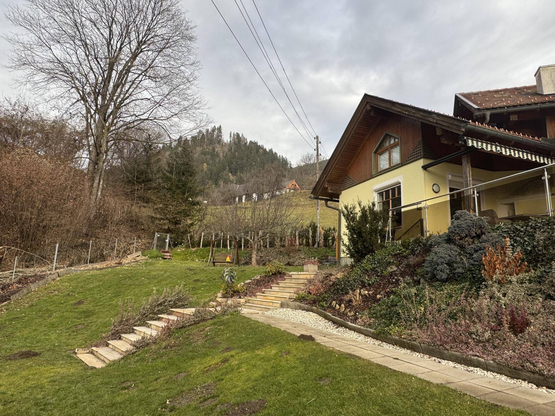 Das Haus in Hanglage mit weitem Blick auf die umliegende grüne Landschaft und die Berge.