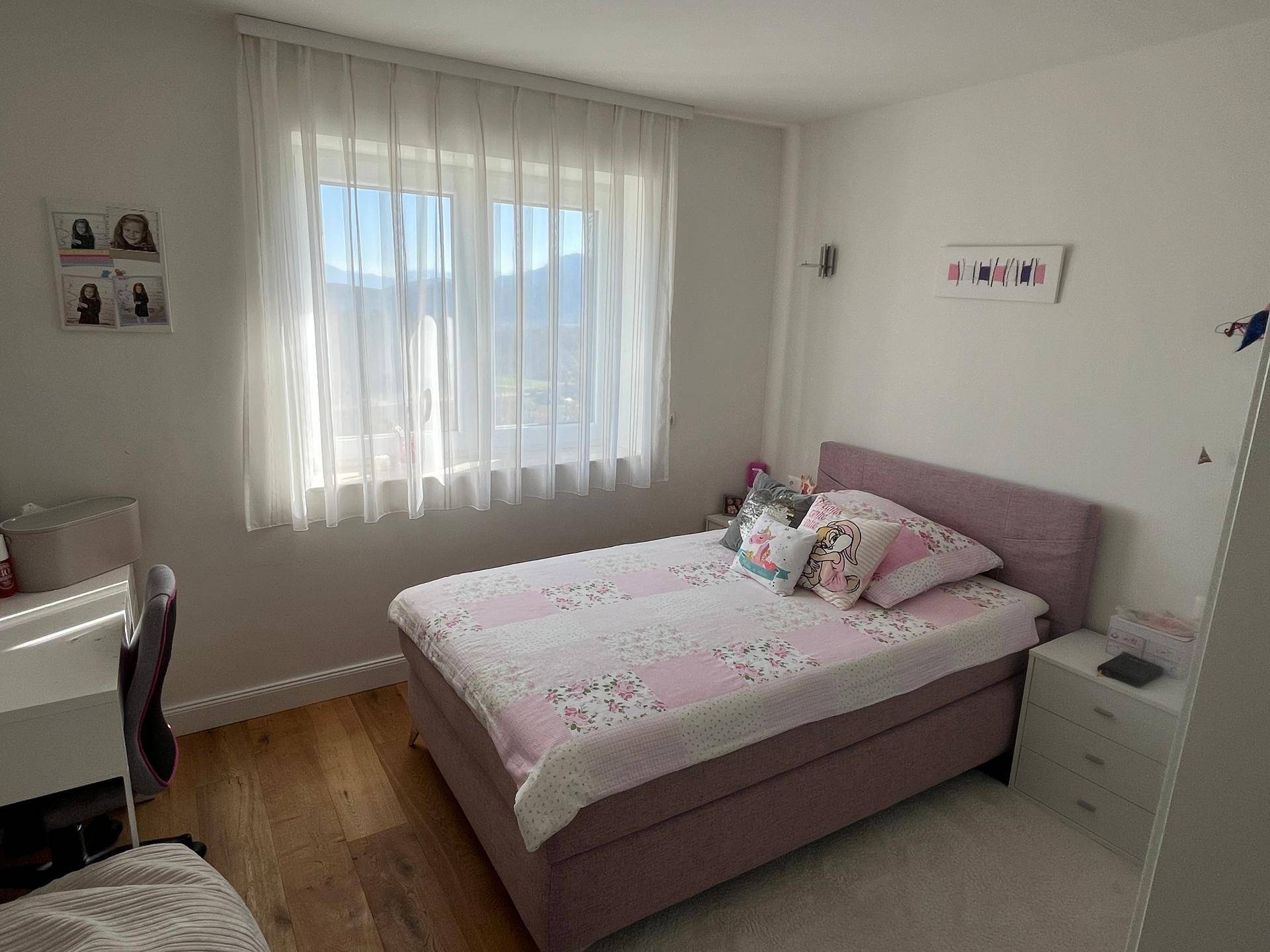 Kinderzimmer mit Einzelbett, Schreibtisch und großem Fenster, das viel Tageslicht hereinlässt.