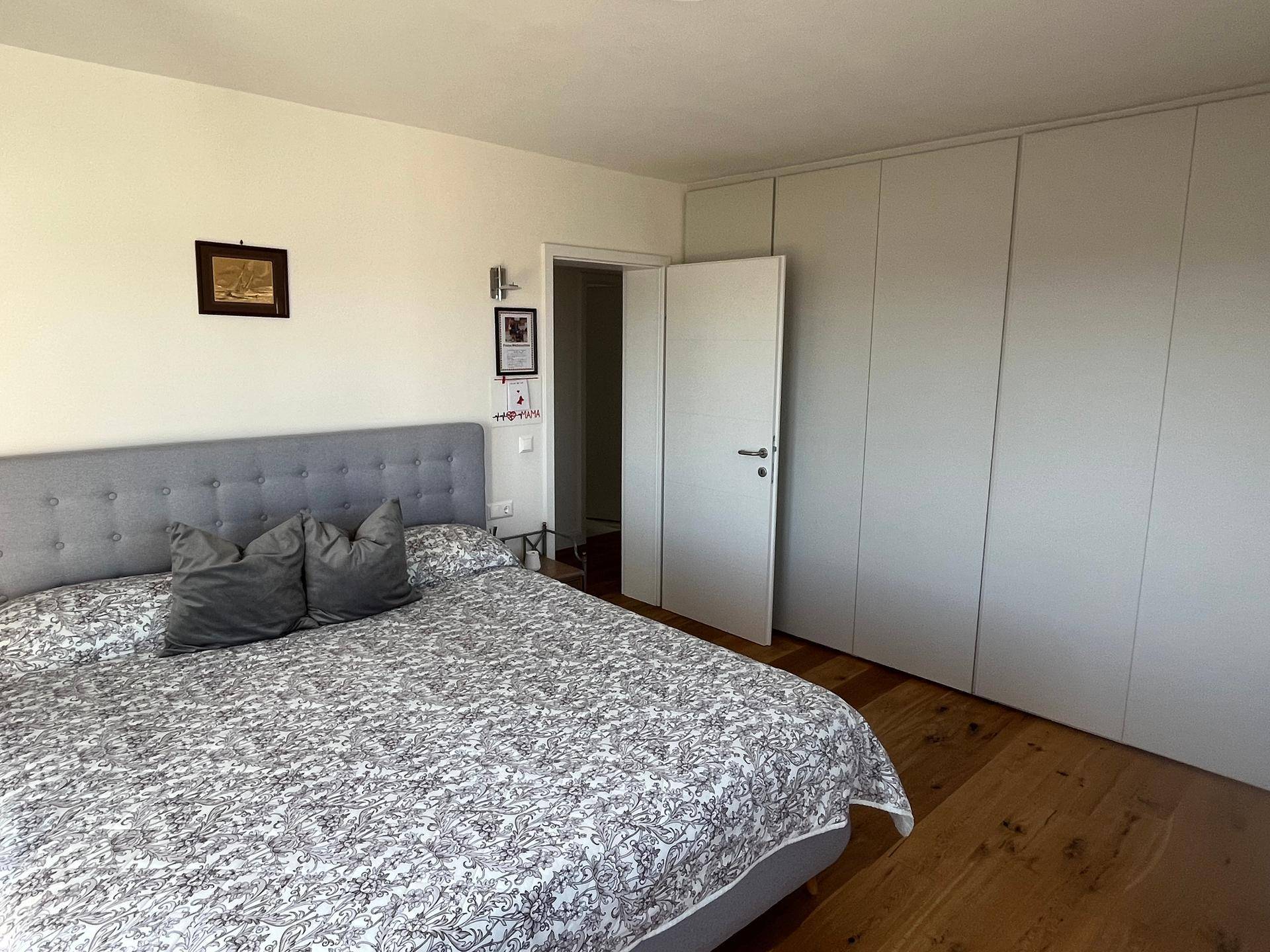 Helles Schlafzimmer mit Holzboden, großem Bett und integrierten Kleiderschränken, bietet viel Stauraum.