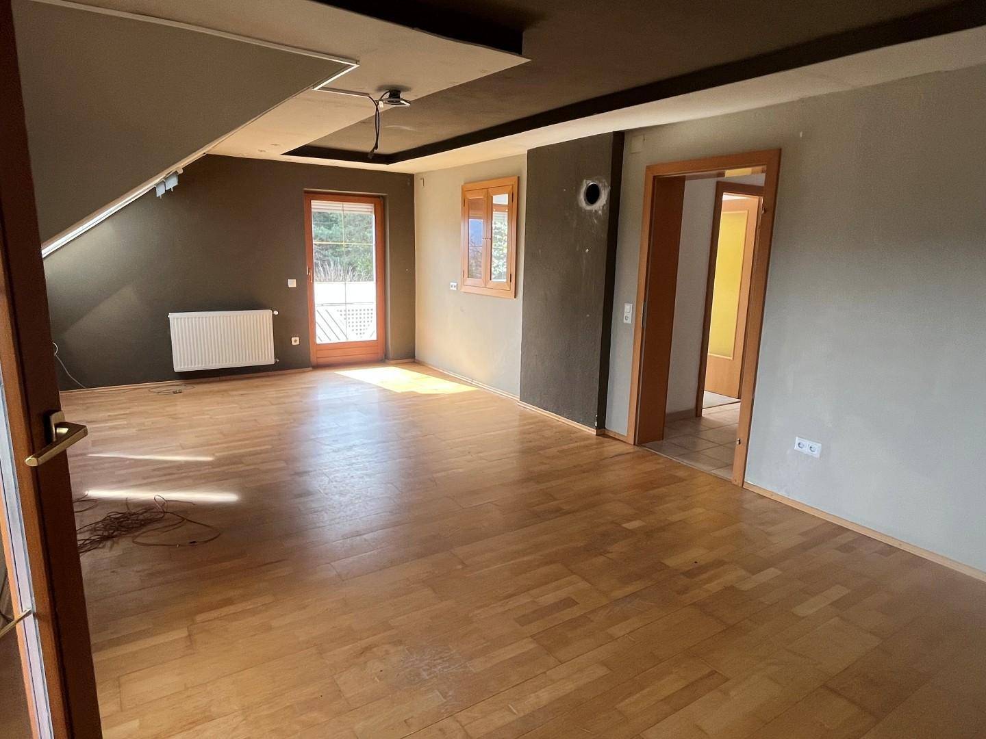 Dachgeschossraum mit Holzboden, dunklen Wänden und Zugang zu einem Balkon.