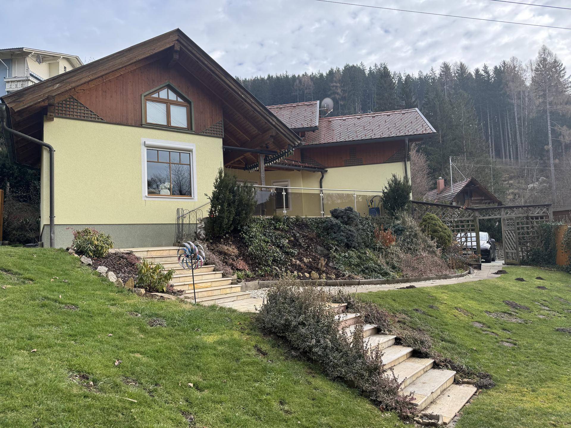 Das charmante Haus mit gelber Fassade und Holzakzenten, umgeben von einem gepflegten Garten und Wald.