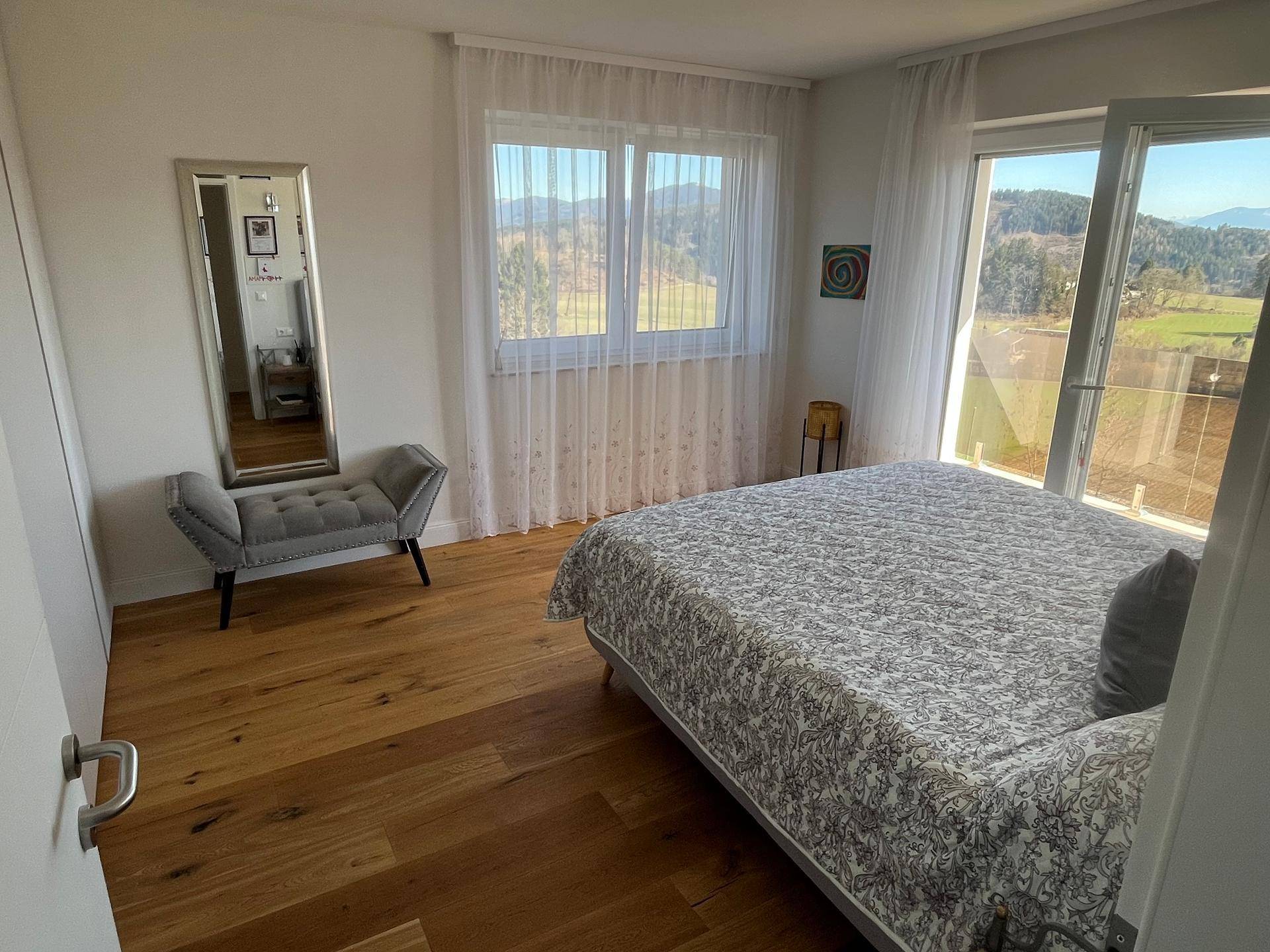 Helles Schlafzimmer mit Holzboden, großem Fenster und Zugang zum Balkon mit Weitblick.