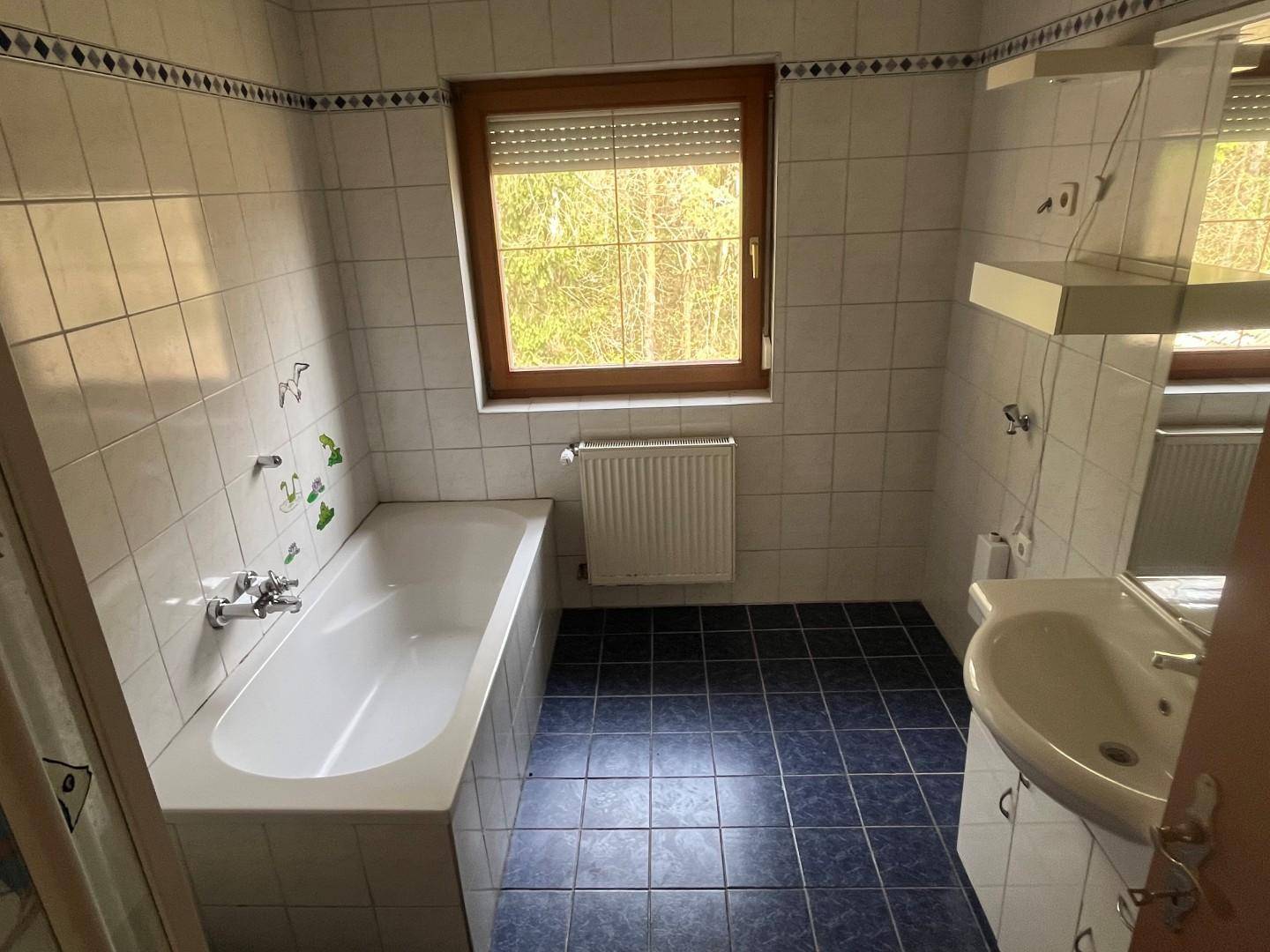Badezimmer mit Badewanne, blauen Fliesen und Fenster für Tageslicht.
