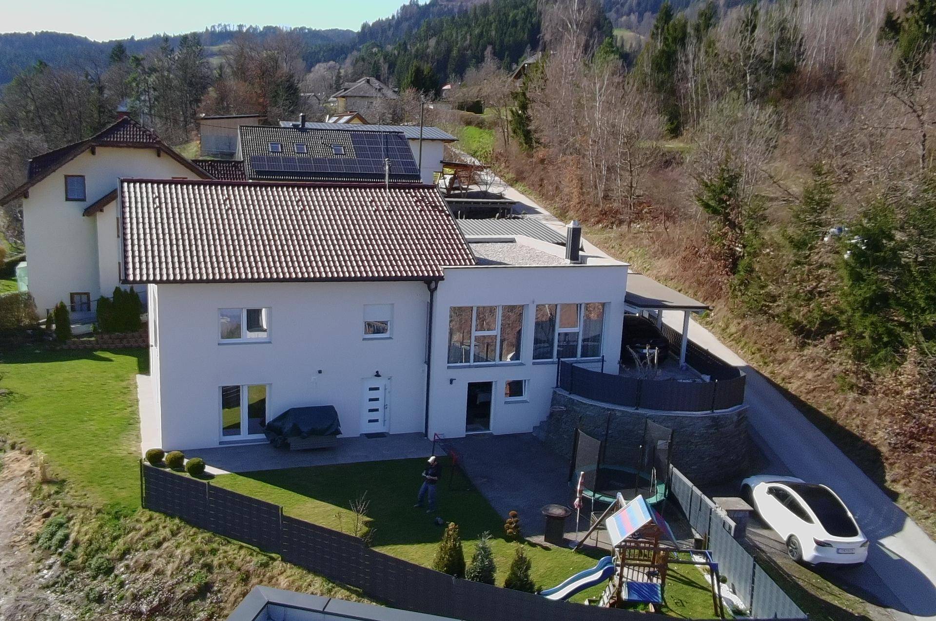 Ansicht des modernen Einfamilienhauses mit Spielplatz im Garten und angrenzender Auffahrt.