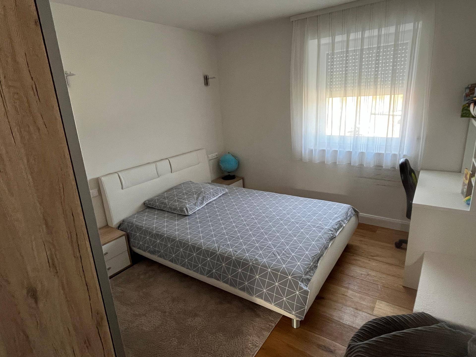 Helles Kinderzimmer mit Holzboden, Einzelbett und einem Schreibtisch direkt am Fenster.