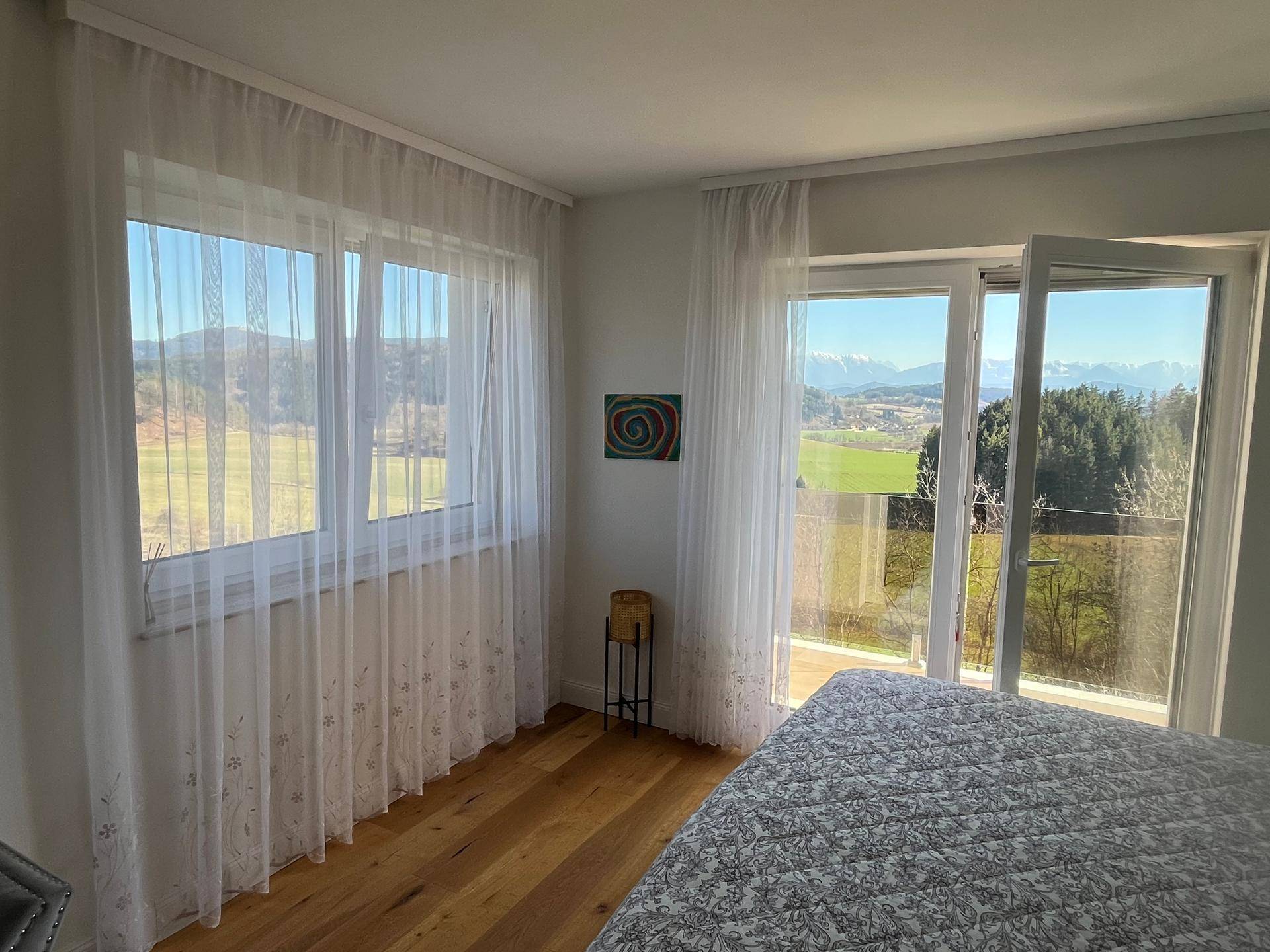 Lichtdurchflutetes Schlafzimmer mit Holzboden, großen Fenstern und Panoramablick auf die Landschaft.