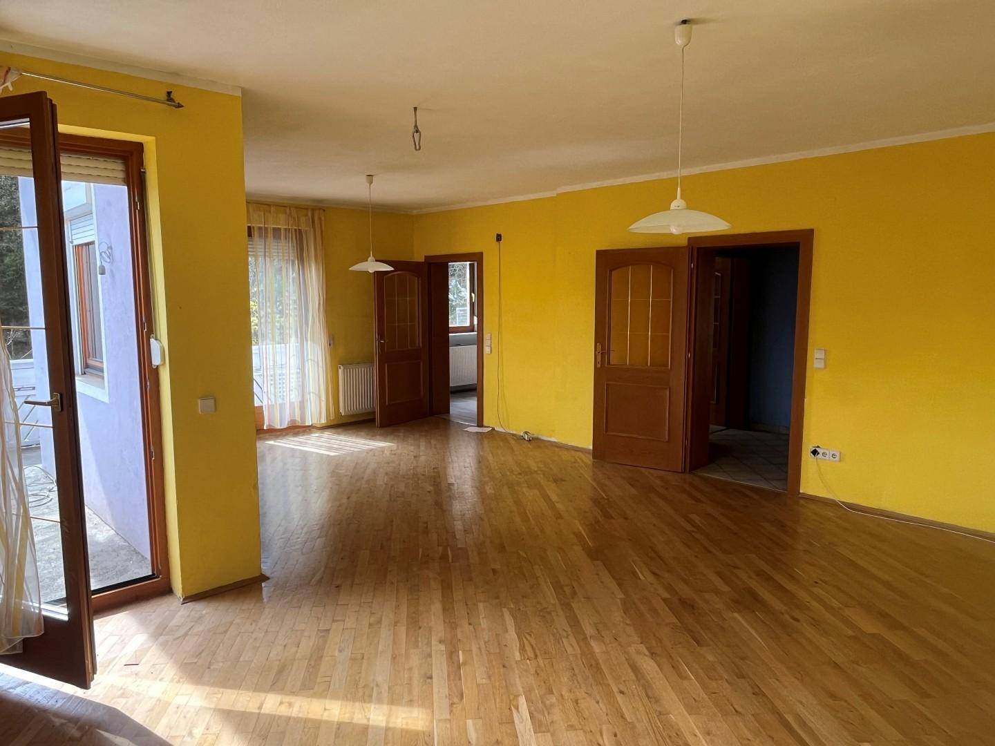 Helles Wohnzimmer mit gelben Wänden, Parkettboden und Zugang zu einem Balkon.