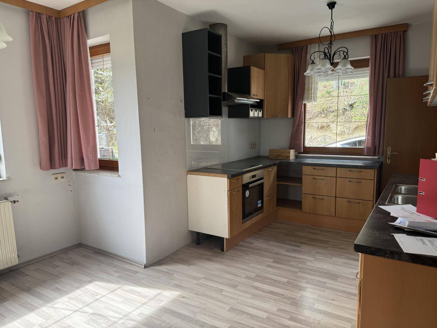 Küche mit Holzschränken, integriertem Backofen und Fenster mit Blick ins Grüne.
