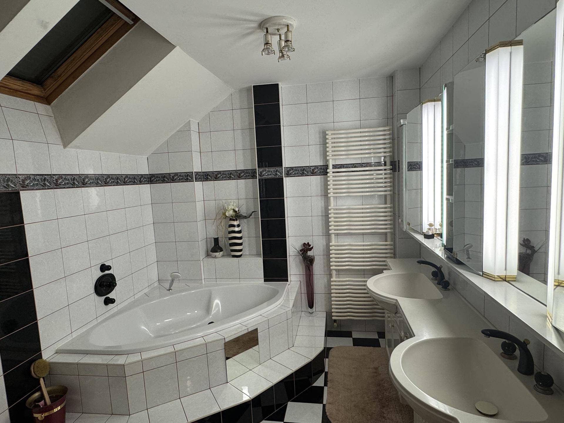 Modernes Badezimmer mit schwarz-weißen Fliesen, Eckbadewanne und Doppelwaschbecken unter Dachschräge.