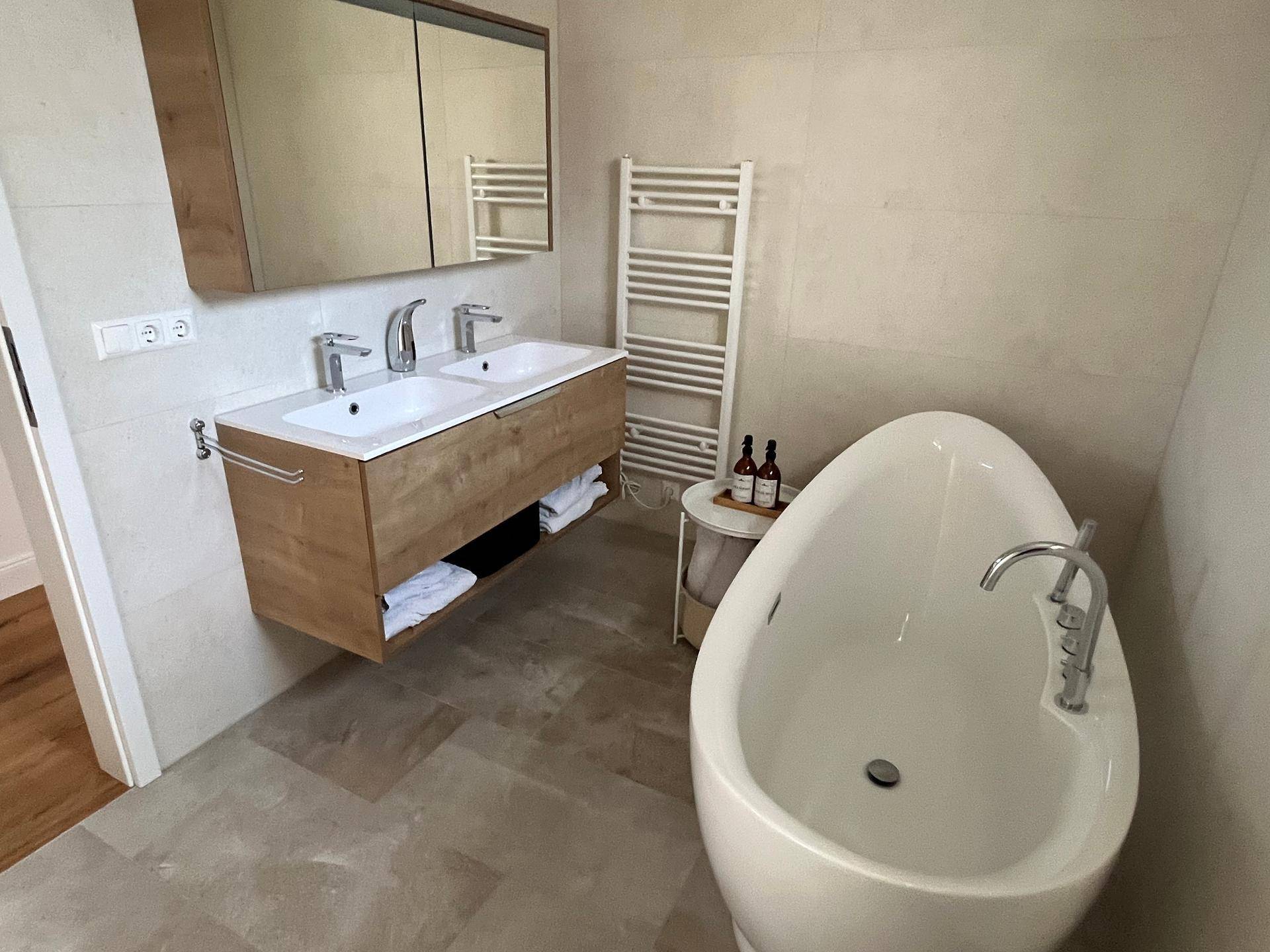 Elegantes Badezimmer mit Doppelwaschbecken, freistehender Wanne und beheiztem Handtuchhalter.