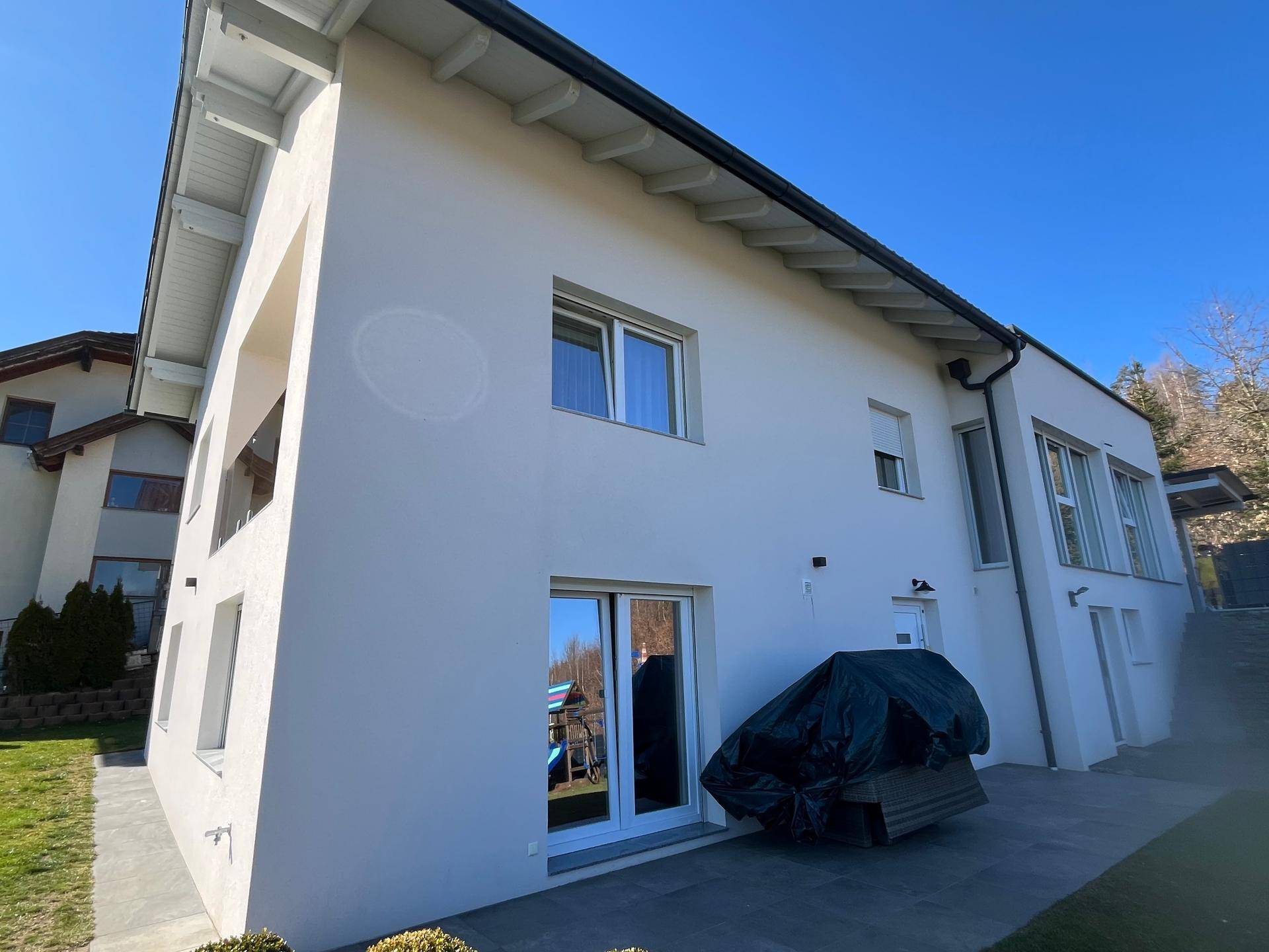 Seitenansicht des modernen Hauses mit weißer Fassade, großen Fenstern und einem kleinen Balkon.