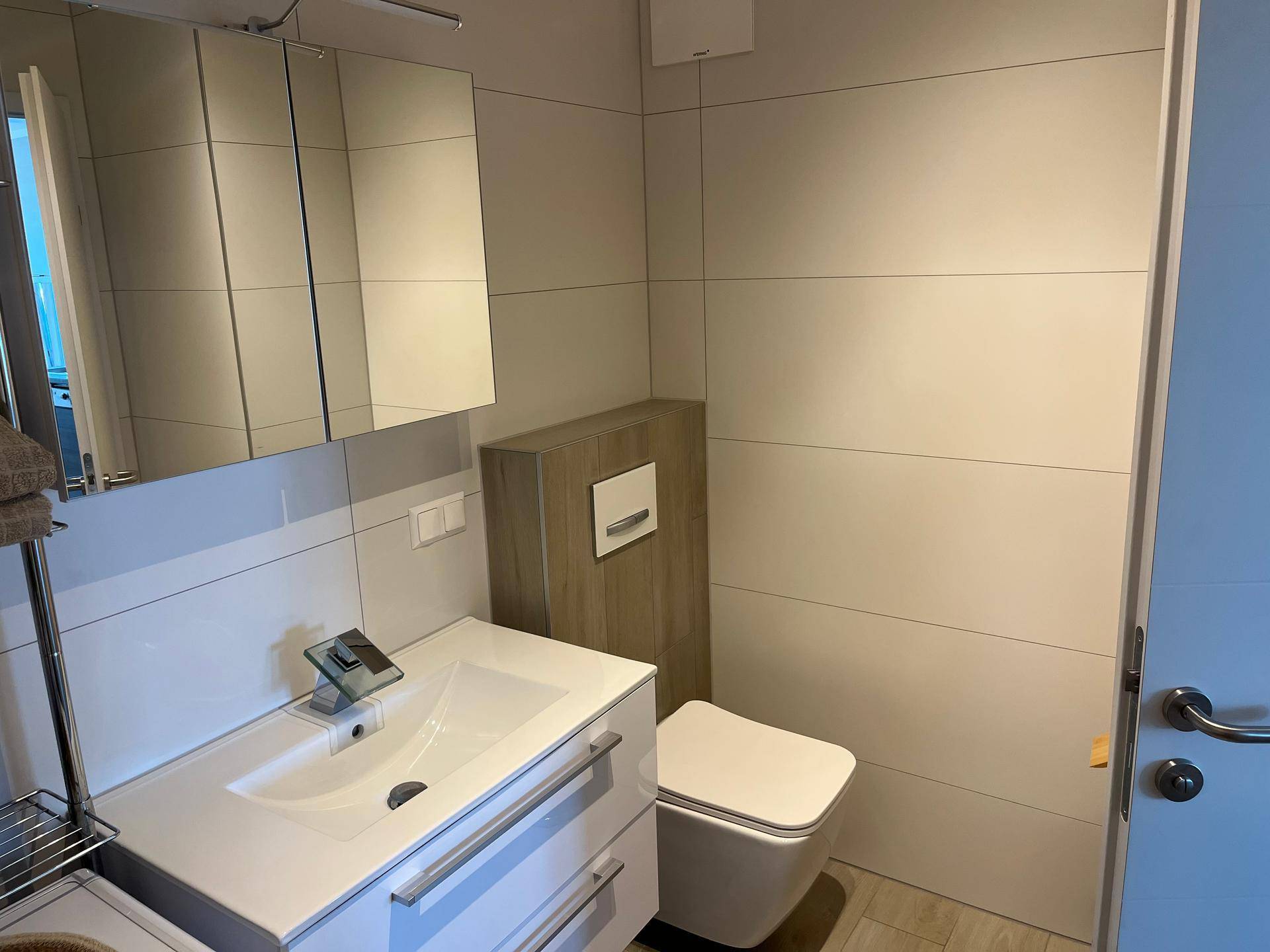 Modernes Badezimmer mit Einzelwaschbecken, Wand-WC und Spiegelschrank.
