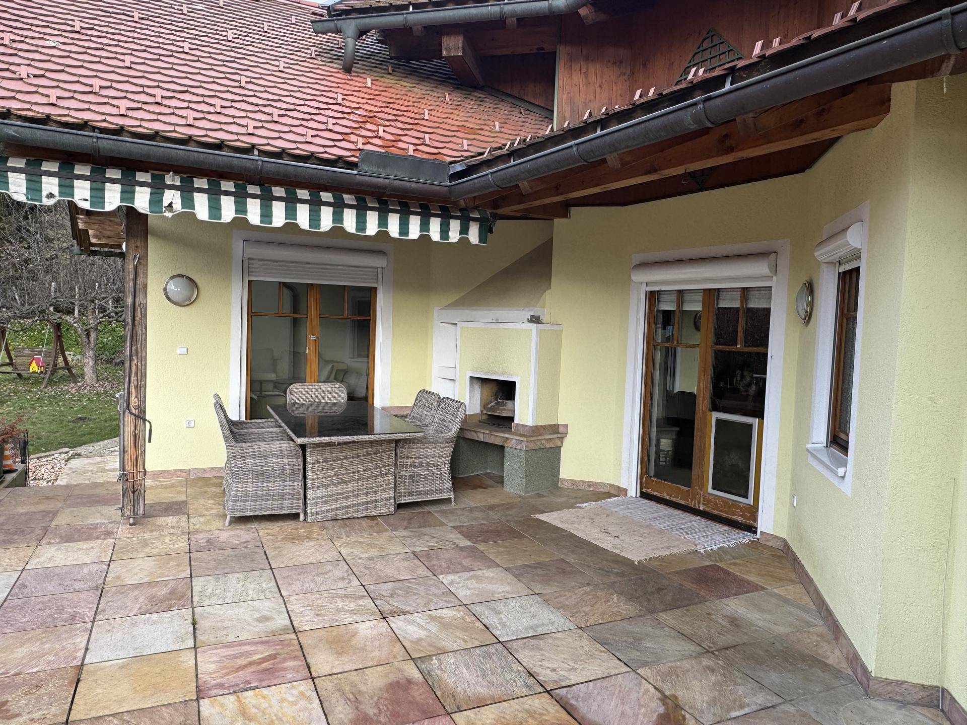 Geräumige Terrasse mit Steinfliesen, Esstisch und Stühlen, ideal für Mahlzeiten im Freien.