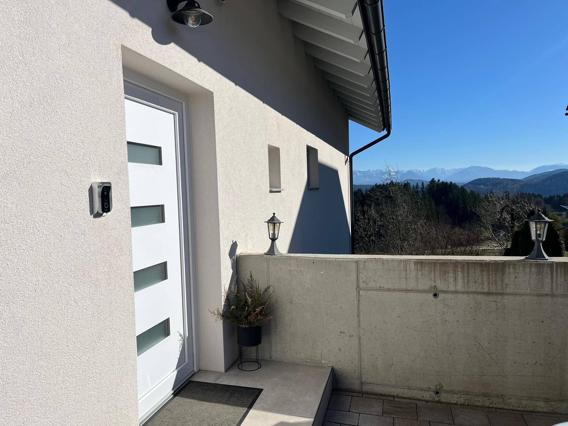 Eingangsbereich des Hauses mit moderner weißer Tür und Blick auf die umliegende Berglandschaft.
