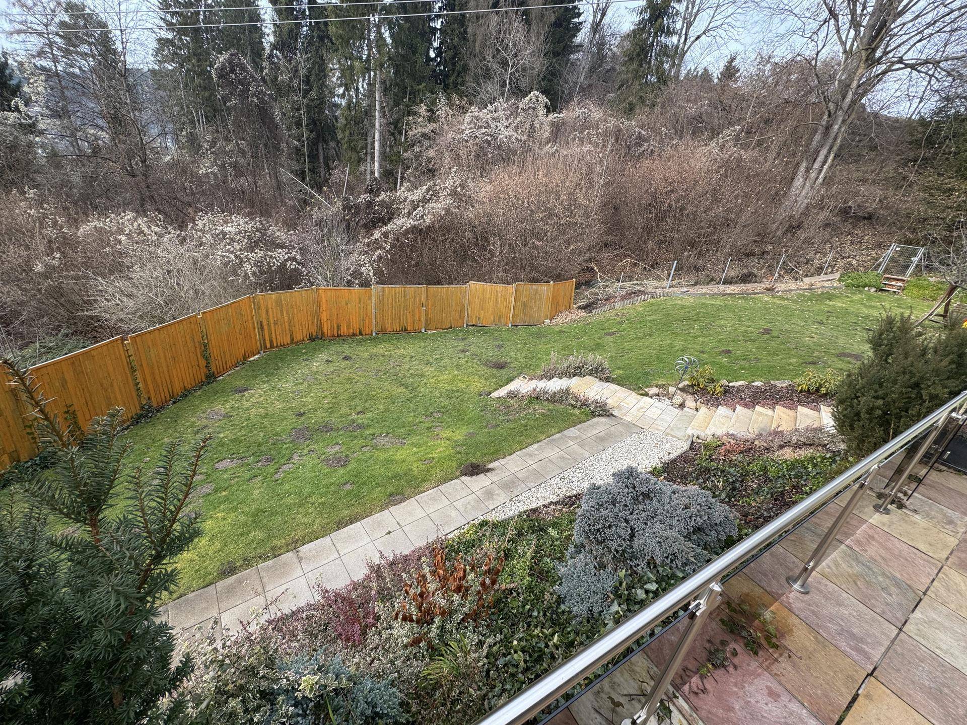 Blick von oben auf den weitläufigen Garten mit Rasenfläche, Gehwegen und einem Holzzaun.
