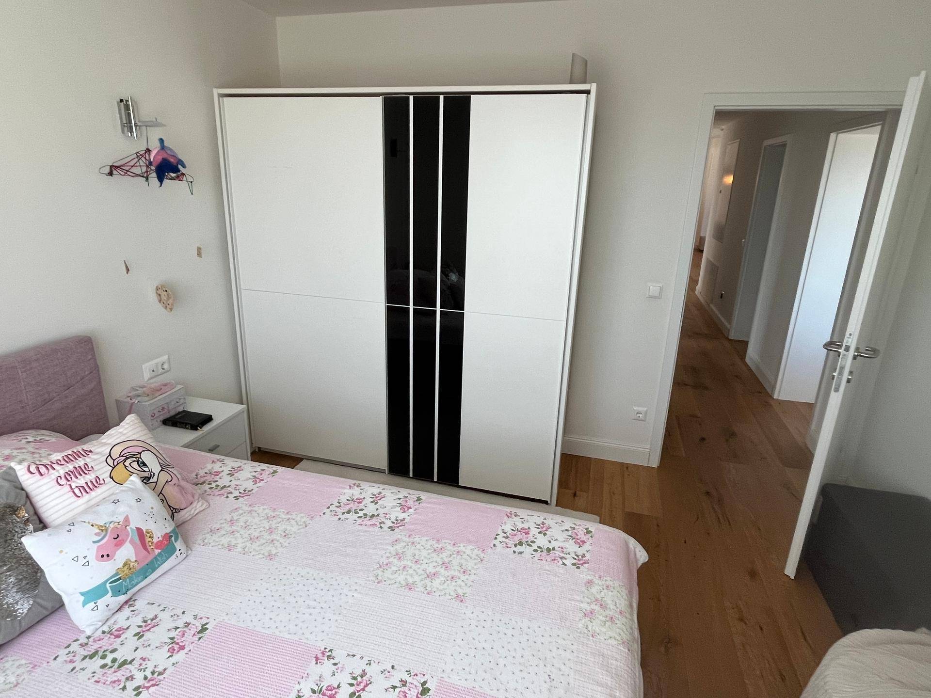 Kinderzimmer mit Einzelbett, modernem Kleiderschrank und Zugang zu einem hellen Flur.