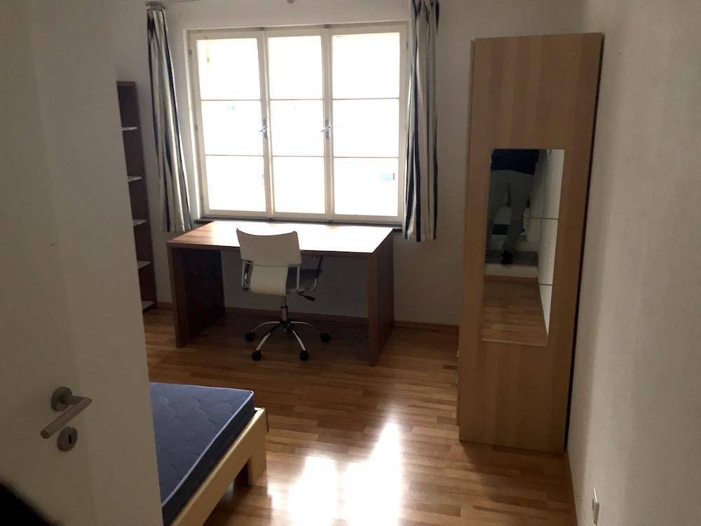 Helles Schlafzimmer mit Schreibtisch, Bürostuhl und einem Kleiderschrank mit Spiegel, ausgestattet mit Parkettboden.