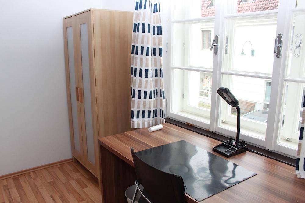 Schlafzimmer mit Schreibtisch am Fenster und einem Kleiderschrank, ausgestattet mit Parkettboden.