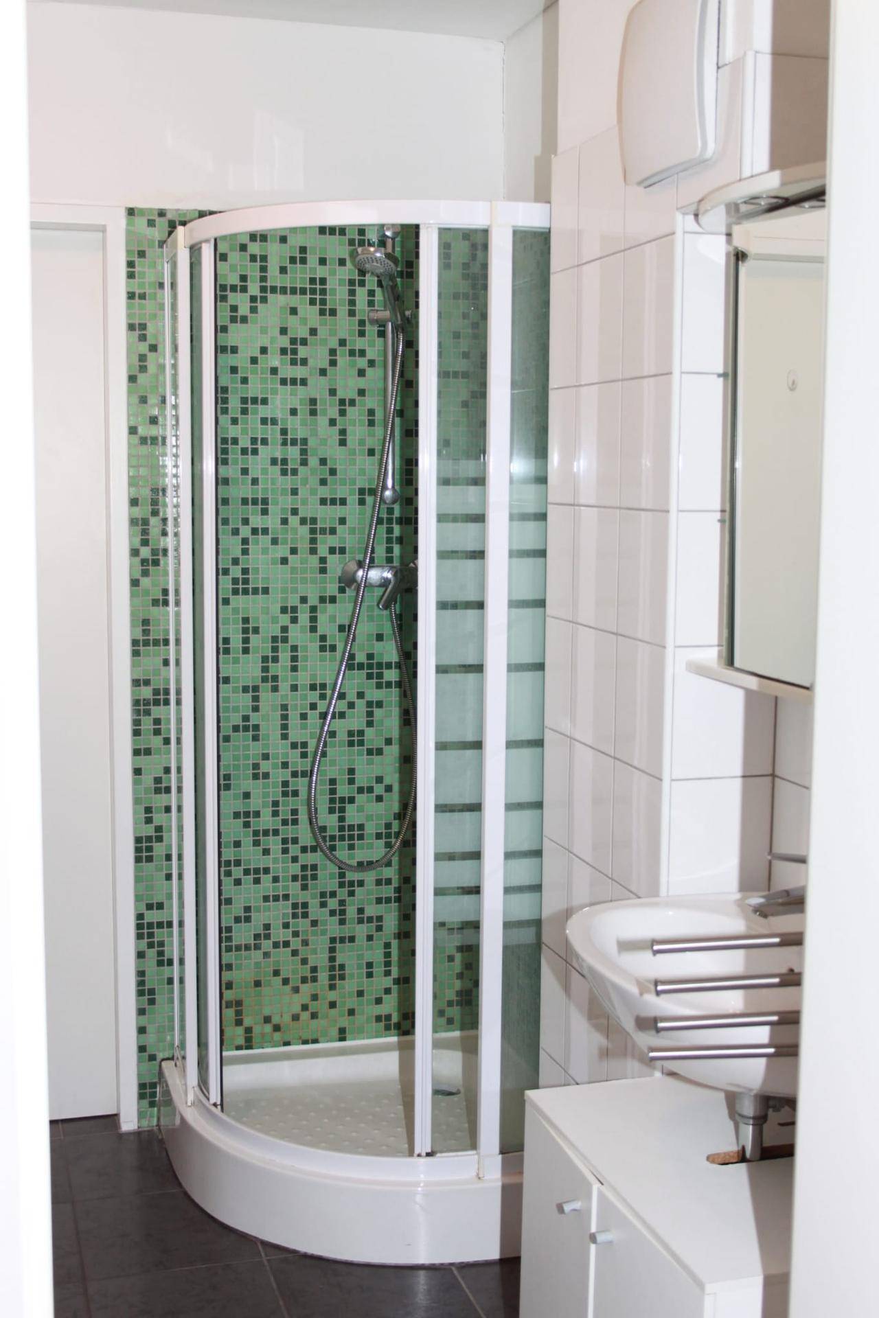 Modernes Badezimmer mit Duschkabine, Waschbecken und grünen Mosaikfliesen an der Wand.