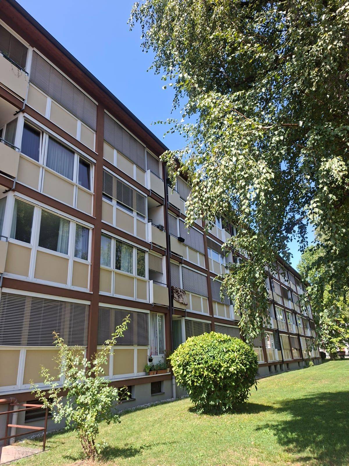 Mehrstöckiges Apartmentgebäude mit Balkonen und grüner Umgebung unter blauem Himmel.