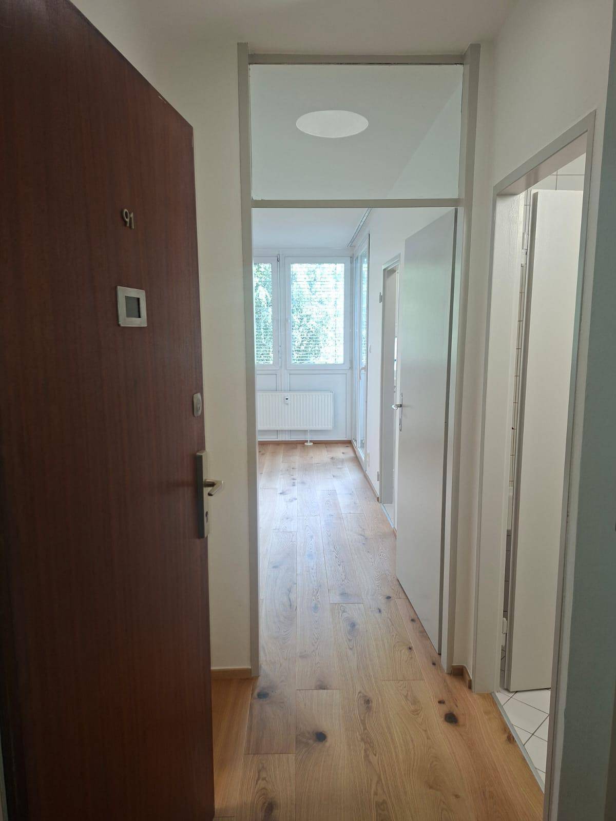 Heller Flur mit Holzboden und mehreren Türen, der zu einem lichtdurchfluteten Raum führt.