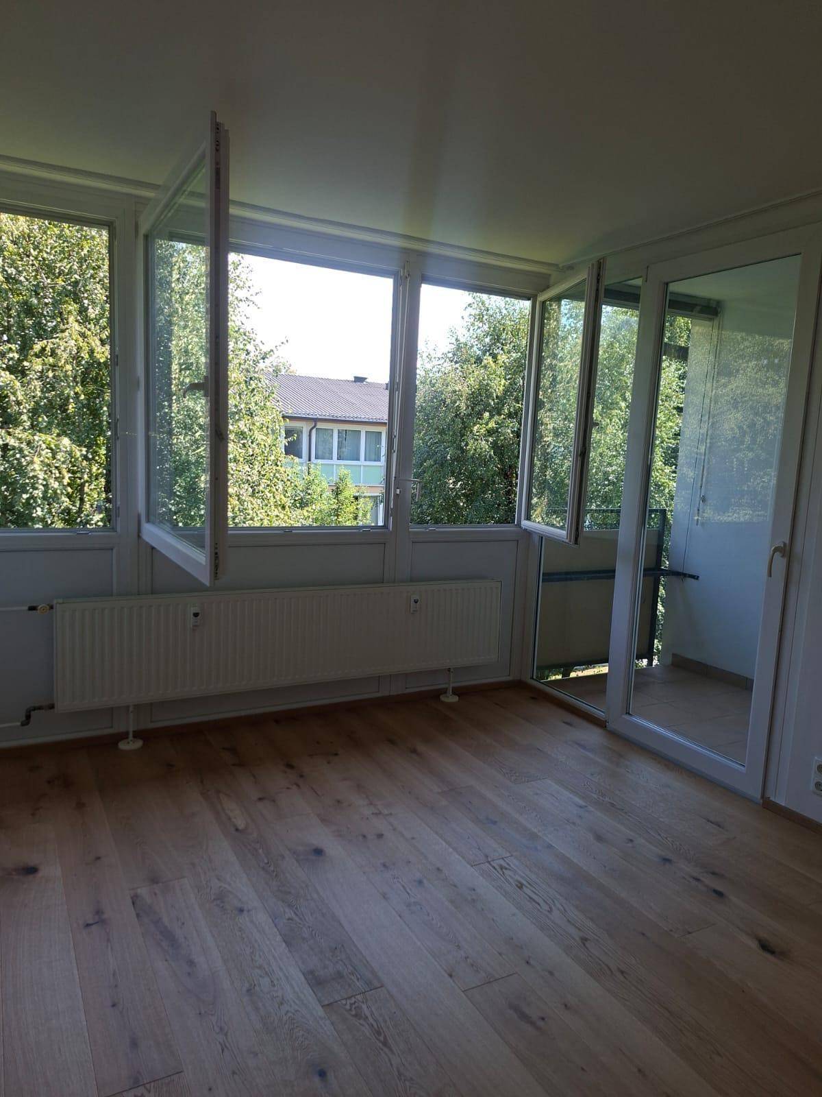 Lichtdurchfluteter Raum mit großen Fenstern, die einen Blick ins Grüne und auf die Umgebung bieten.
