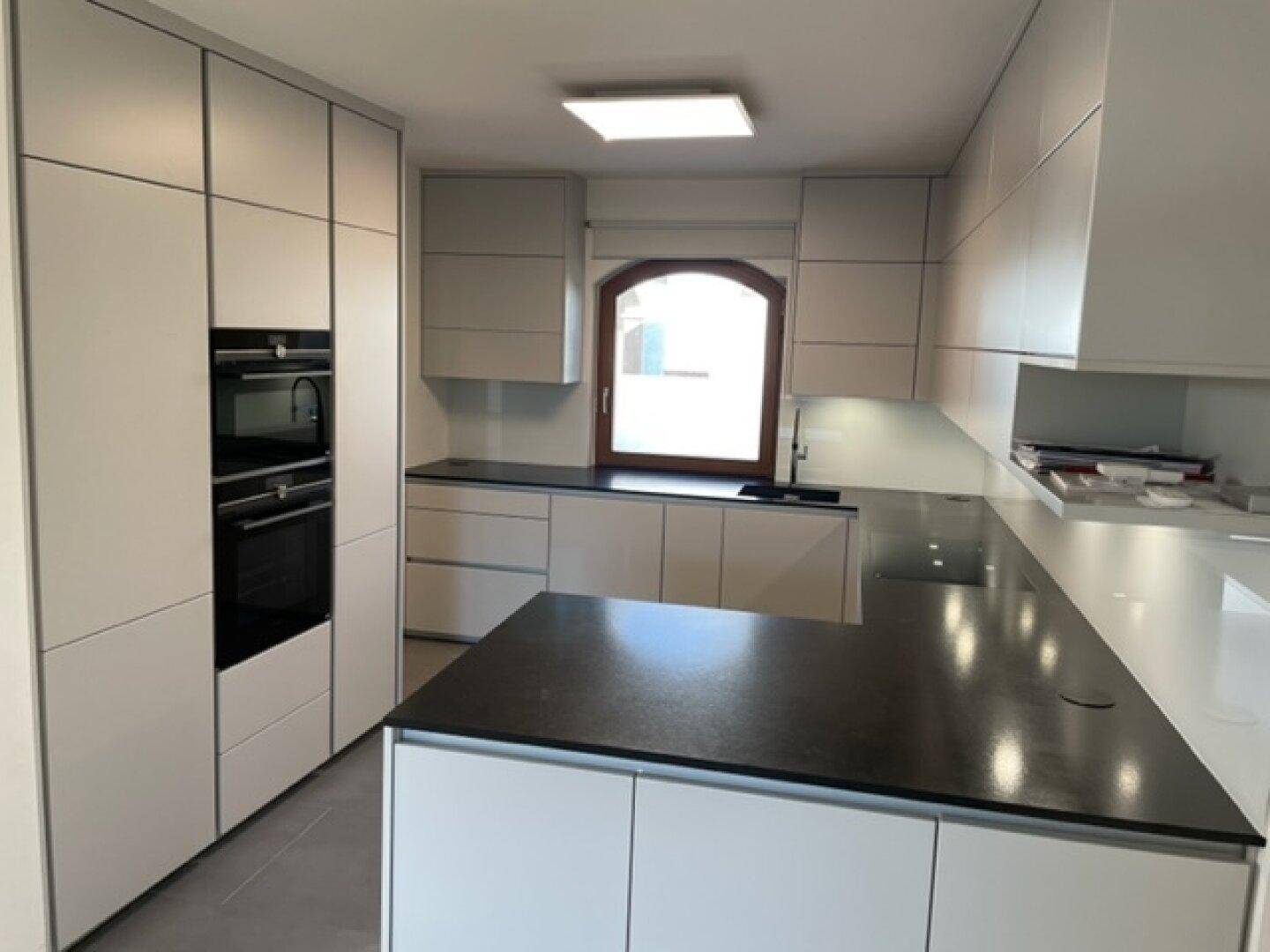 Moderne Küche mit hellen Schränken, dunklen Arbeitsplatten und integrierten Geräten.