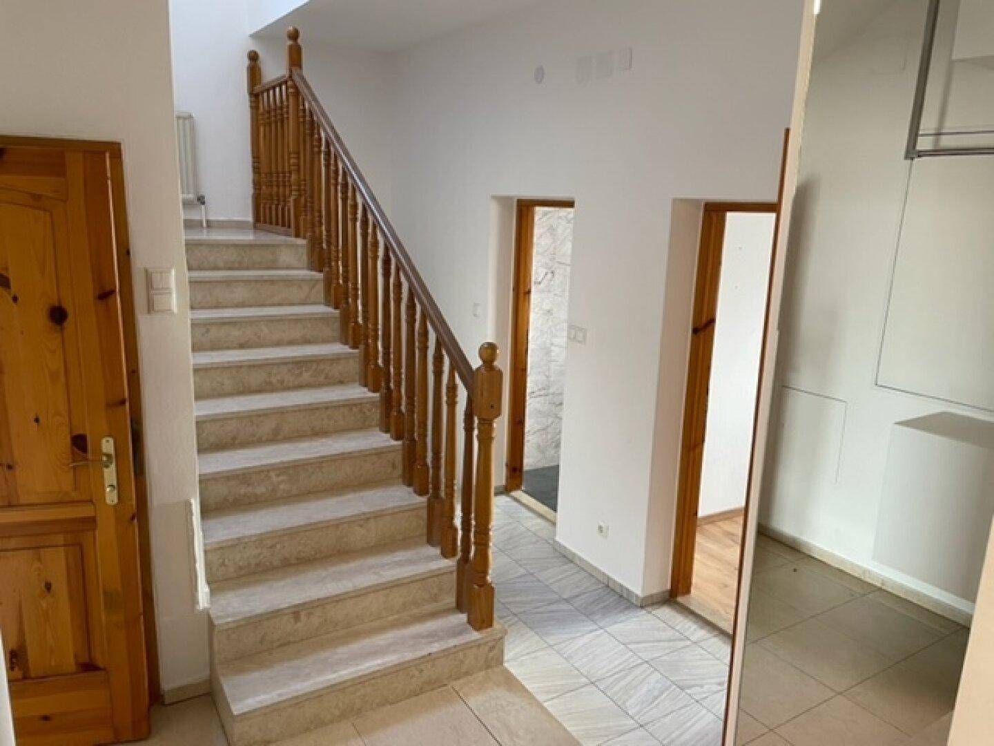Heller Flur mit Steintreppe, Holzgeländer und Holztüren.