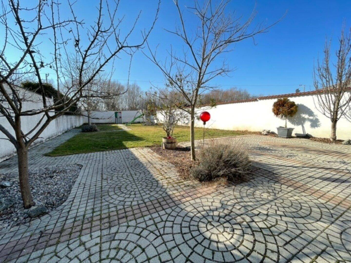 Gepflegter Gartenbereich mit Rasenfläche, gepflastertem Weg und hohen Mauern.