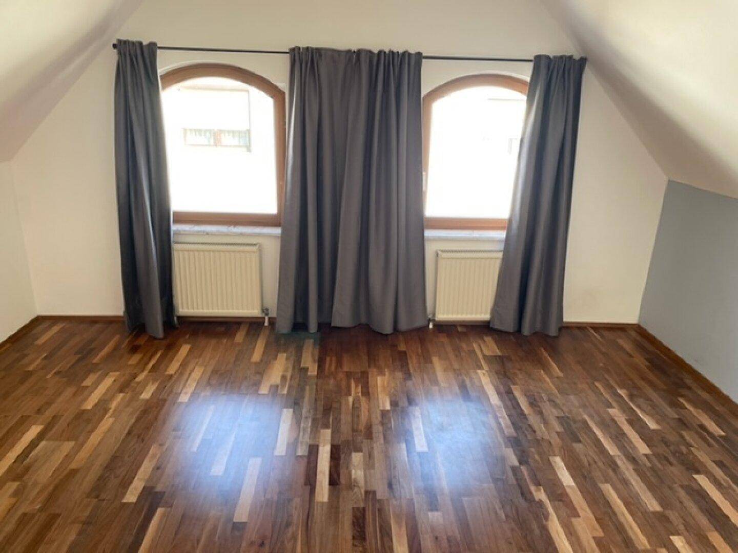 Schlafzimmer mit Holzboden, zwei Bogenfenstern und Dachschrägen.