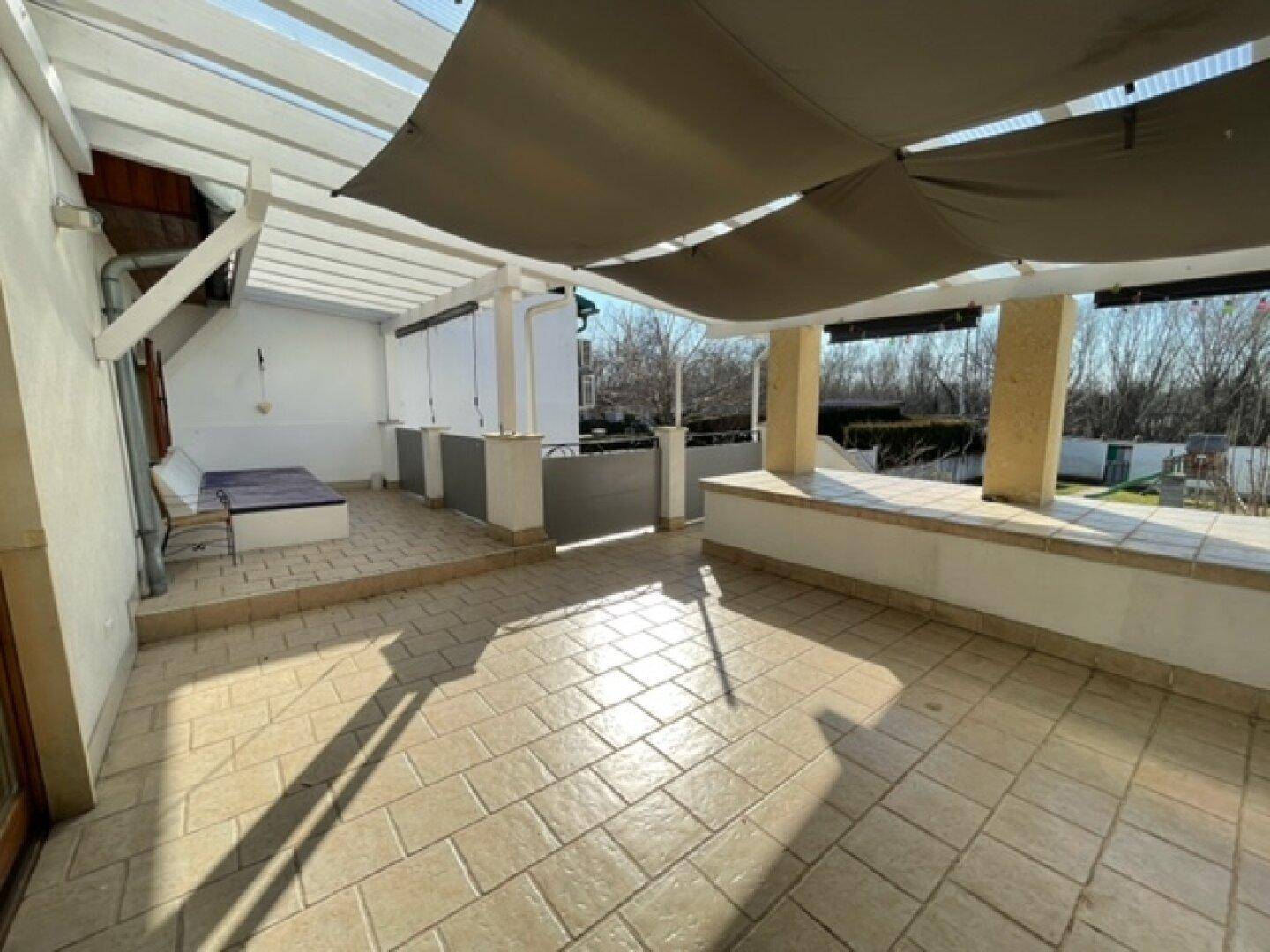 Geräumige Außenterrasse mit Sonnenschutz, Fliesenboden und Blick ins Grüne.