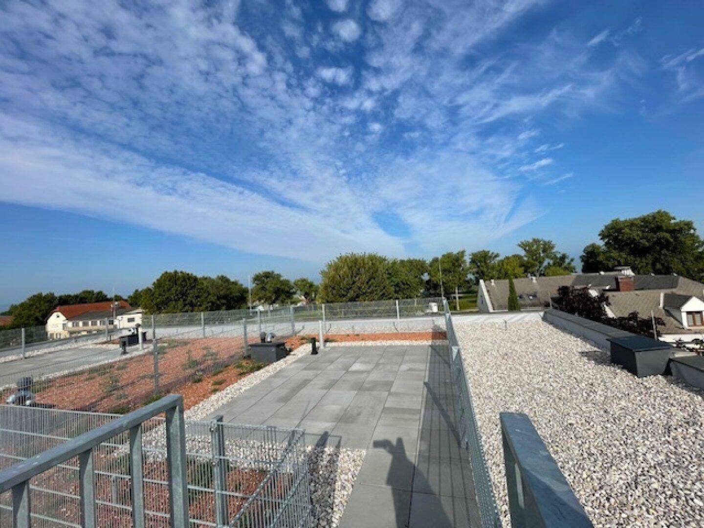 Weitläufige Dachterrasse mit Fliesen und Kiesbereichen, umgeben von einer weiten Aussicht.