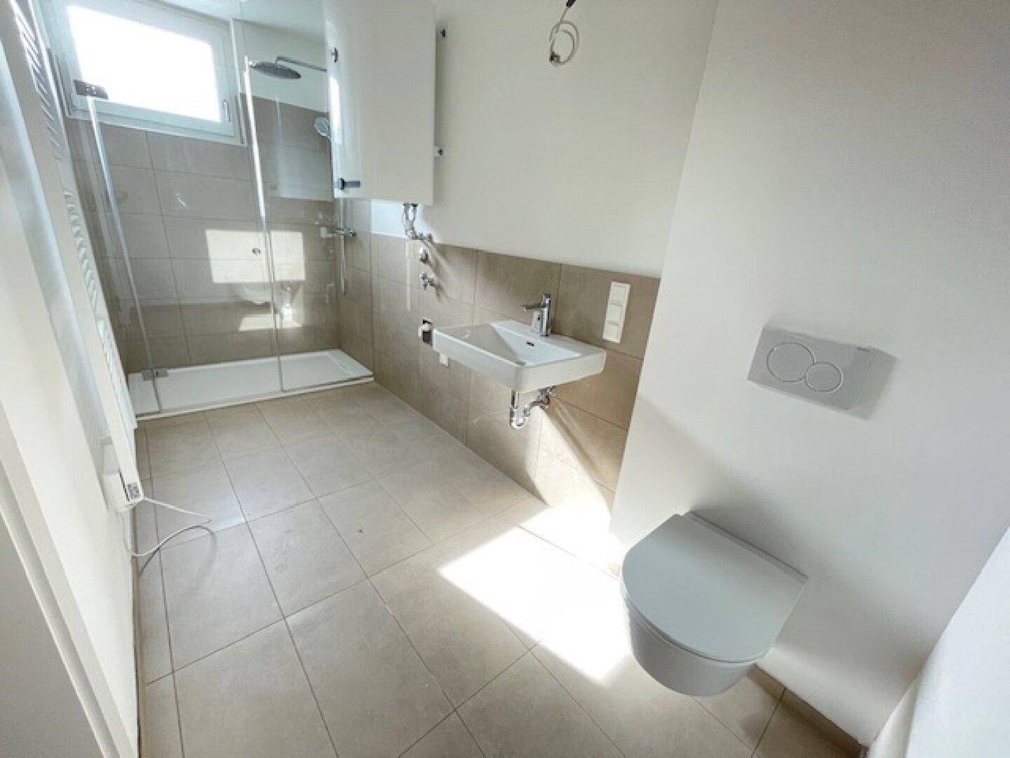 Modernes Badezimmer mit Dusche, WC und Waschbecken, ausgestattet mit hellen Fliesen.