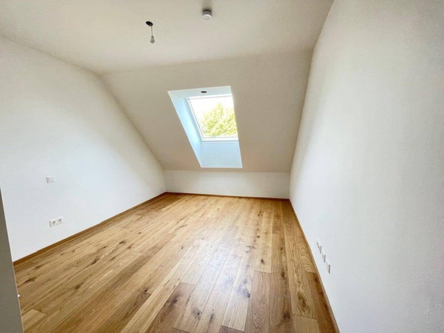 Lichtdurchflutetes Zimmer mit Holzboden und Dachschräge, beleuchtet durch ein großes Dachfenster.