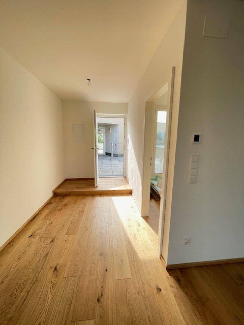 Heller Flur mit Holzboden und weiß gestrichenen Wänden, der zu weiteren Räumen führt.