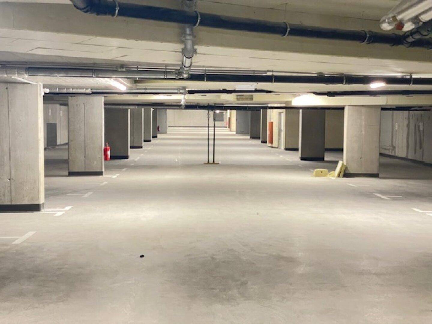 Geräumige Tiefgarage mit Betonpfeilern und markierten Stellplätzen, gut beleuchtet.