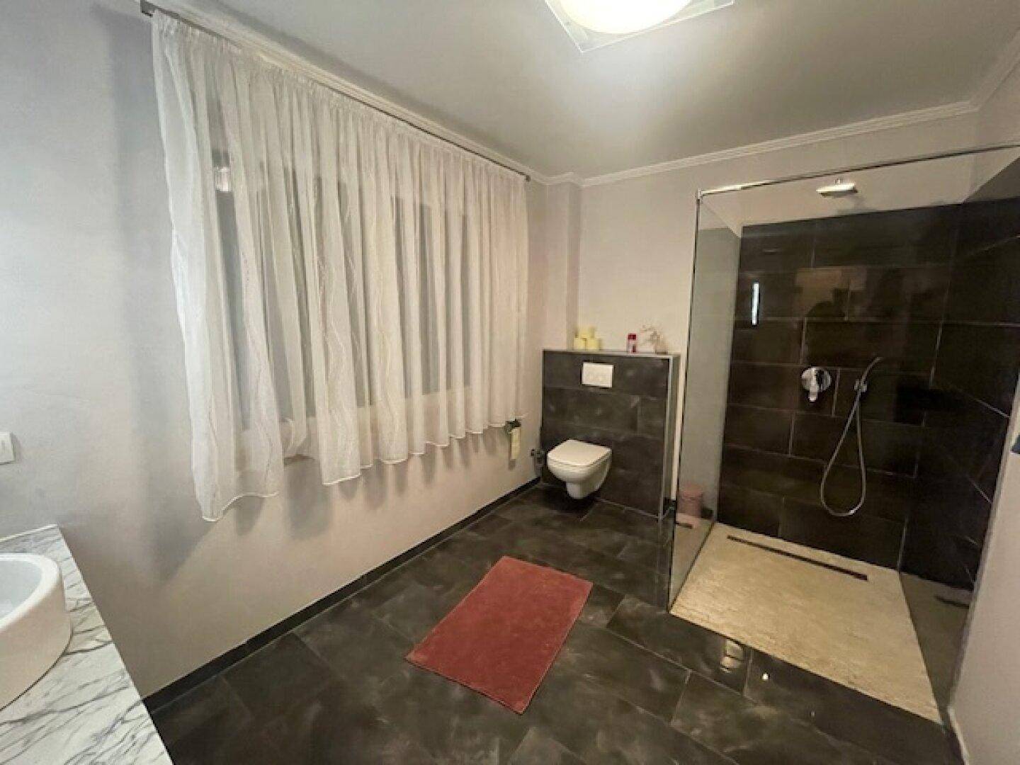 Modernes Badezimmer mit ebenerdiger Dusche, Wand-WC und Fenster.