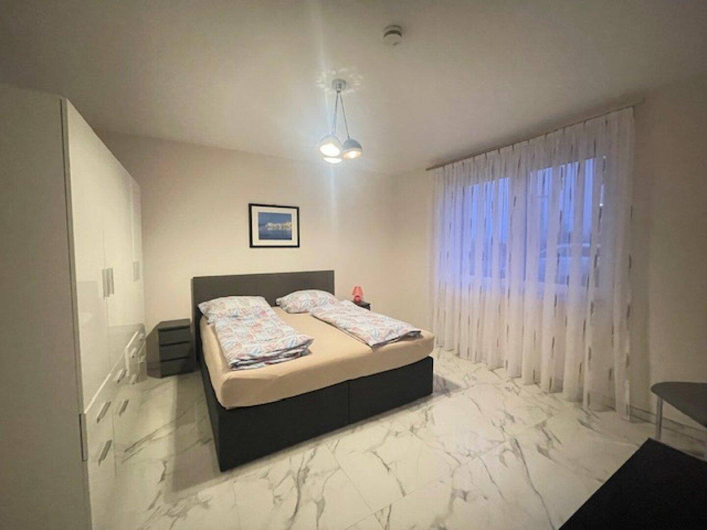 Schlafzimmer mit großem Bett, weißen Schränken und modernen Fliesenboden.